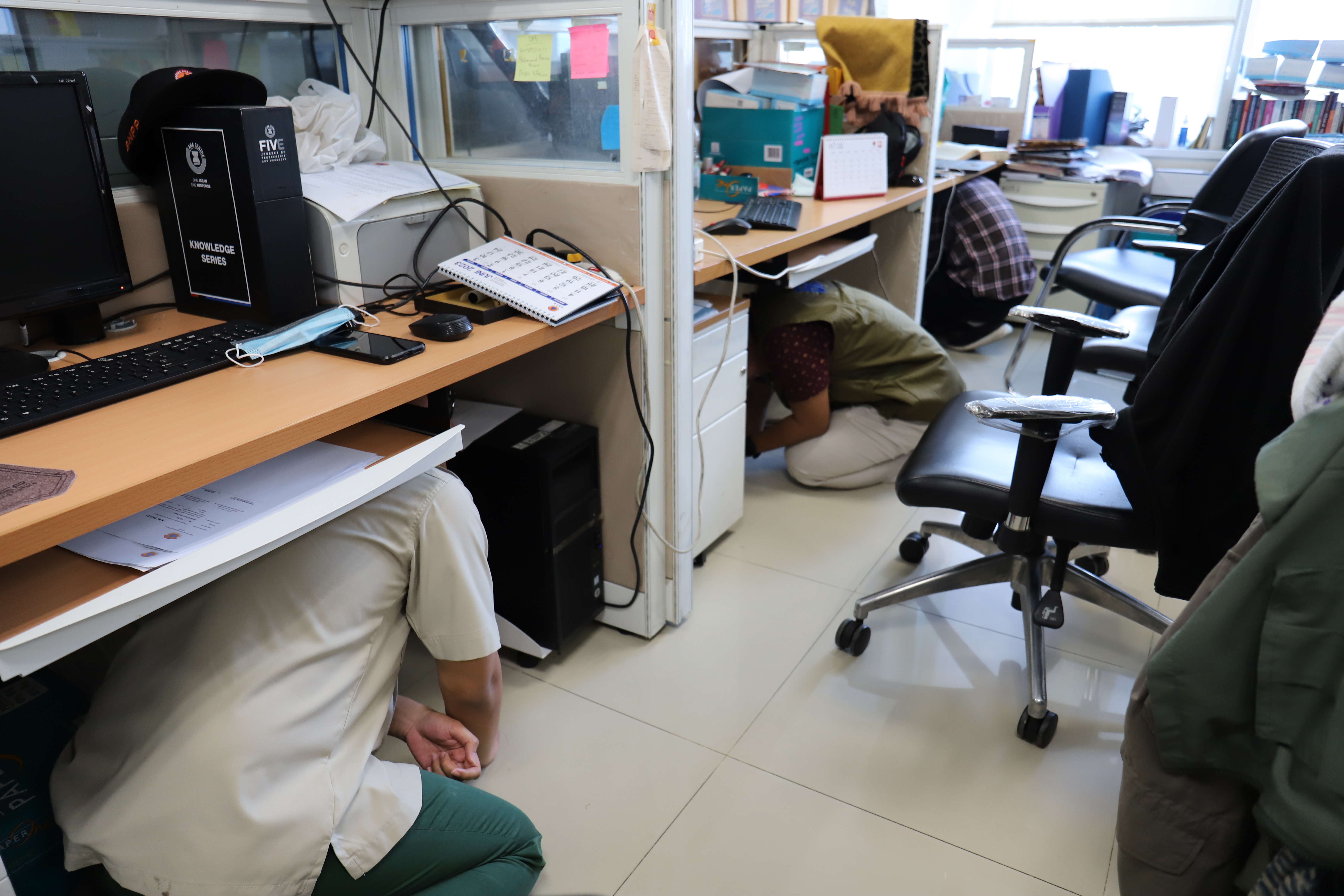 Para pegawai berlindung dibawah meja, sesaat sebelum keluar menuju titik kumpul, saat simulasi evakuasi bencana gempa di Gedung Graha BNPB, Jakarta pada Rabu (26/4).